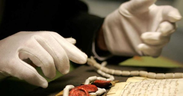 Une paire de mains gantées de blanc manipule un document ancien aux Archives nationales du Royaume-Uni. © The National Archives (UK).
